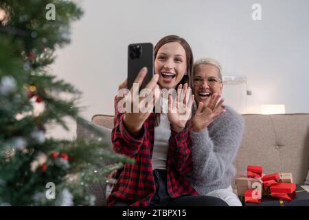 Feiern Sie Weihnachten, Silvester, Mutter und Tochter halten ein Smartphone-Selfie und machen Sie Fotos, grüßen Sie während der sozialen Distanz per Videoanruf Stockfoto