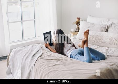 Entzückendes Mädchen aus den 12er Jahren in kabellosen Kopfhörern, das mit einem digitalen Tablet auf dem Bett liegt. Junge Generation und moderne Technologie-Überbeanspruchung, Gadget-Nutzung für Stockfoto