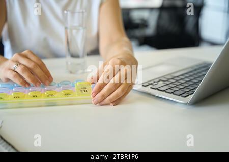 Frau an ihrem Arbeitsplatz nimmt Pillen aus dem Pillen-Organisator Stockfoto