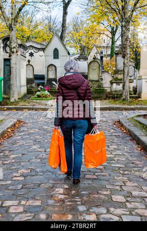 Paris, Frankreich. Reife Erwachsene Frau, die auf dem Friedhof Pere Lachaise mit orangefarbenen Einkaufstaschen unterwegs ist. Stockfoto