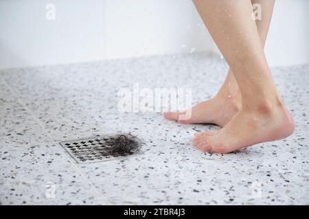 Eine Frau, die unter Alopezie leidet, duscht, im Abfluss sind Haare neben ihren Füßen Stockfoto