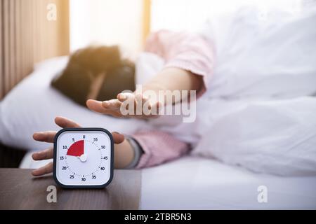 Eine Frau, die eine Augenklappe trägt, versucht, den Timer zu berühren, während sie aufwacht Stockfoto