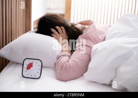 Eine Frau, die eine Augenklappe trägt, versucht, den Timer zu berühren, während sie aufwacht Stockfoto