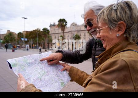 Fröhliches Seniorenpaar, das zusammen eine Papierkarte sucht, um während ihrer Reise nach einem Ort zu suchen. Stockfoto