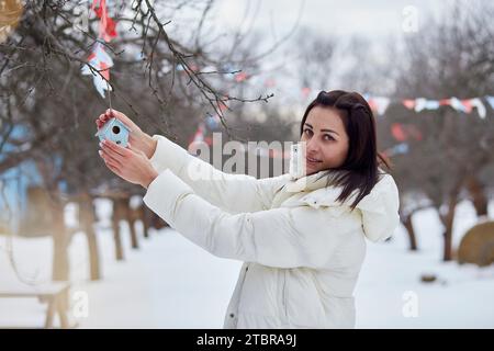 Frau, die den Haushof mit handgefertigten Spielzeugen schmückt. Winterwetter draußen. Saisonale Traditionen. Stockfoto