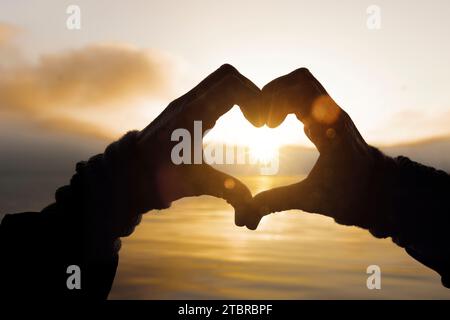 Zwei Hände bilden ein Herz vor einem See bei Sonnenuntergang Stockfoto