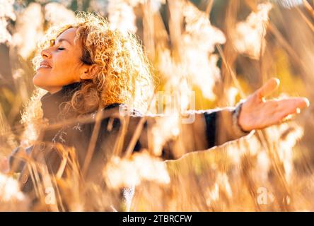 Eine glückliche Frau, die Arme ausstreckt und die Natur genießt, die im goldenen Feld mit Sonnenuntergang lächelt. Menschen und Freizeitaktivitäten im Freien. Glück und Wohlbefinden Lifestyle Lady. Freiheit. Das Leben ist überglücklich Stockfoto