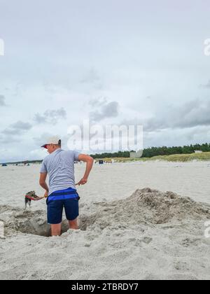Deutschland, Mecklenburg-Vorpommern, Halbinsel Fischland-Darß-Zingst, Prerow, ein Teenager steht in einem Sandloch am Strand mit einer Schaufel Algen in der Hand Stockfoto