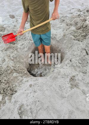 Deutschland, Mecklenburg-Vorpommern, Halbinsel Fischland-Darß-Zingst, Prerow, ein Teenager steht in einem Sandloch am Strand mit einer Schaufel in der Hand Stockfoto
