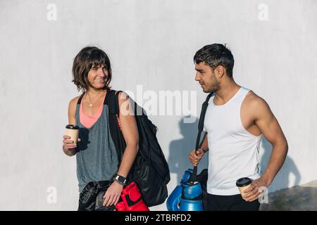 Ein horizontales Foto von Freunden, die mit Sportkleidung, Rucksack, Boxhandschuhen und Kaffee zum Mitnehmen in der Hand in Richtung Fitnessstudio gehen. Auf weißem Hintergrund Stockfoto