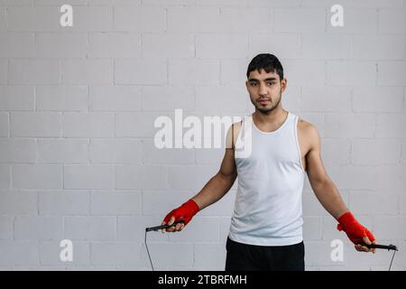 Horizontaler Fotomann, junger Erwachsener, gemischtes Race-Springseil, mit roten Boxhandschuhen in den Händen. Auf weißem Hintergrund für den Kopierbereich. Sport- und Freizeitangebote Stockfoto