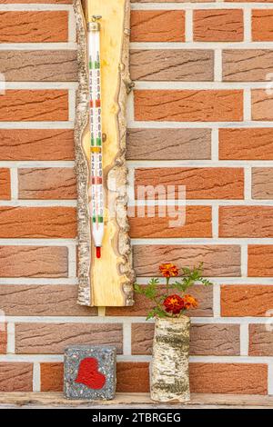 Altes Quecksilberthermometer im Holzrahmen an einer Hauswand, dekorative Vase mit Blumen, Stein mit rotem Herz Stockfoto