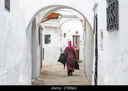 Marokkanische muslimische Frau in traditioneller islamischer Kleidung in Hijab, die mit Einkaufstaschen in der Medina der Stadt Tétouan / Tettawen, Marokko, wandert Stockfoto