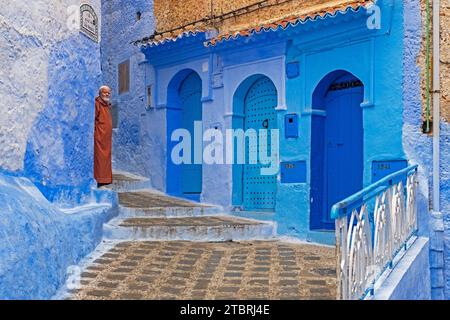 Muslimischer Mann mit traditioneller Djellaba in einer Gasse mit blauen Häusern und Türen in Medina / historischer Altstadt Chefchaouen / Chaouen, Marokko Stockfoto