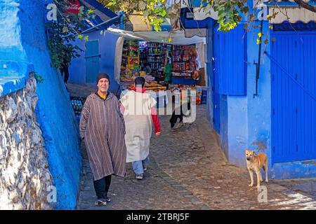 Muslimischer Mann mit traditioneller Djellaba und Lebensmittelgeschäft in der Gasse in der blauen Medina / historische Altstadt der Stadt Chefchaouen / Chaouen, Marokko Stockfoto