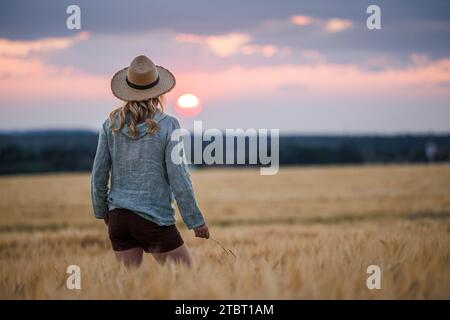 Zufriedener Landwirt schaut sich Gerstenfeld in der Bio-Farm an. Frau, die während des Sonnenuntergangs auf dem landwirtschaftlichen Feld steht Stockfoto