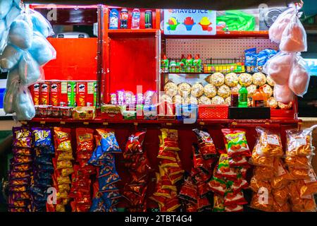 Farbenfroher Snackkarren am Abend mit Zuckerwatte, Chips, Popcorn, rasiertem Eis und Limonaden Stockfoto