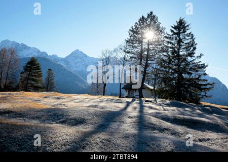 Kapelle hinter Bäumen im Hintergrund mit Karwendelbergen im Hintergrund bei Mittenwald, Oberbayern, Bayern, Deutschland Stockfoto