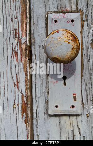 Nahaufnahme des verwitterten Türknopfs und der alten Holztür mit Abziehfarbe Stockfoto