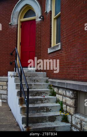 Klassischer Eingang mit roter Tür im Backsteingebäude mit schmutziger weißer Treppe Stockfoto