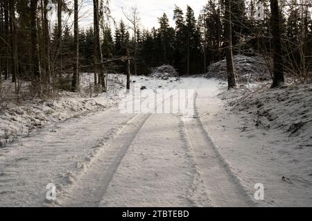 Die Straße zeugt von Reifenspuren, leisen Geschichten von Abenteuern durch schneebedeckte Wälder unter dem goldenen Touch der Sonnenstrahlen. Stockfoto