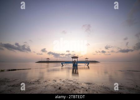 Morgenlandschaft auf einem Sandstrand, Blick über das Meer bis zum Horizont mit kleinen Tempeln im Wasser und einem Jukung, ein traditionelles Fischerboot im Meer, Sonnenaufgang in Sanur, Bali, Indonesien Stockfoto