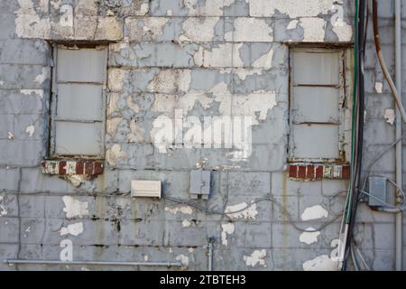Nahaufnahme der altersgrauen Betonwand mit elektrischen Kabelkanälen und verwitterten Fenstern Stockfoto