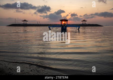 Morgenlandschaft auf einem Sandstrand, Blick über das Meer bis zum Horizont mit kleinen Tempeln im Wasser und einem Jukung, ein traditionelles Fischerboot im Meer, Sonnenaufgang in Sanur, Bali, Indonesien Stockfoto