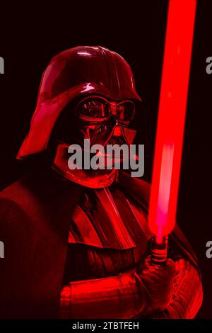 NEC, BIRMINGHAM, GROSSBRITANNIEN - 3. DEZEMBER 2023. Ein männliches Cosplay bei einem Comic-Concept-Event in Darth Vader Kostüm aus Star Wars mit einem roten Lichtschwert in einem Drama Stockfoto