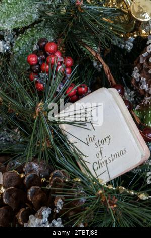 Die wahre Weihnachtsgeschichte in einem kleinen weißen Buch mit einem Stern an der Spitze wird auf künstlichen Zweigen mit stechpalmenbeeren und Tannenzapfen gezeigt. Stockfoto