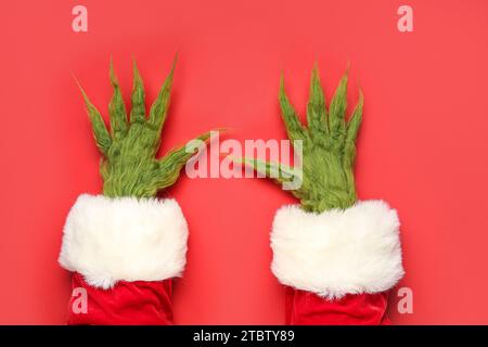 Haarige Hände einer grünen Kreatur im Weihnachtsmannkostüm auf rotem Hintergrund Stockfoto