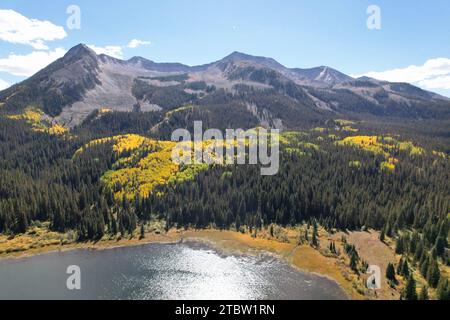 Ein ruhiger See, umgeben von üppigen grünen Bäumen und dramatischen Berggipfeln im Hintergrund Stockfoto