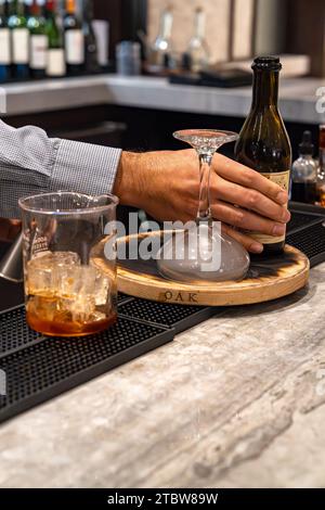 Der Barkeeper schnappt sich eine Flasche Wermut und bereitet mit einem Glasbecher und einem umgedrehten Cocktailglas einen geräucherten Whiskey-Cocktail-Drink zu Stockfoto