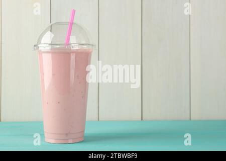 Leckerer Smoothie im Plastikbecher auf hellblauem Tisch vor weißer Holzwand. Leerzeichen für Text Stockfoto