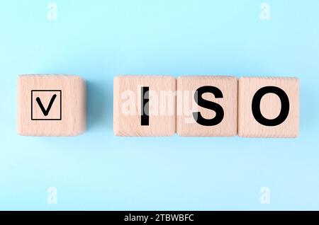 Internationale Organisation für Normung. Holzwürfel mit Häkchen und Abkürzung ISO auf hellblauem Hintergrund, flache Lagen Stockfoto