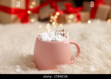 Weihnachtskakao mit Marshmallows und Lebkuchenkeks in rosa Tasse auf weichem Teppich drinnen, Nahaufnahme Stockfoto