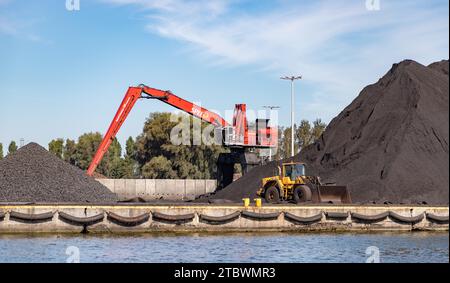 Ein Bild von einem Kran und einem Planierraupen neben großen Kies- und Kohlestapeln in der Danziger Werft Stockfoto