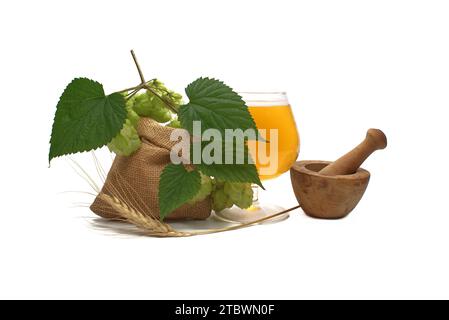 Bier- oder Getränkestillleben mit einem Zweig grünem Hopfen und Gerste, der aus einem hessischen Beutel verschüttet wird, zusammen mit einem eleganten Glas gekühlten Lagers oder vom Fass Stockfoto