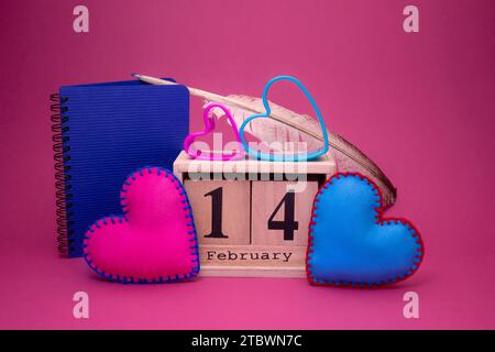 Stillleben zum Valentinstag mit handgenähten rosa und blauen Herzen aus Textil, die ein hölzernes Datum mit passenden herzförmigen Ausstechern flankieren Stockfoto