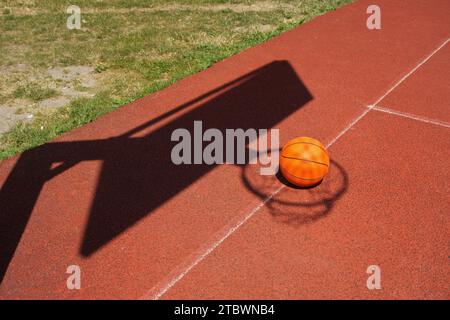 Basketball auf einem Hof im Schatten des Net und Torpfosten in einem konzeptionellen Bild mit Kopie Raum Stockfoto