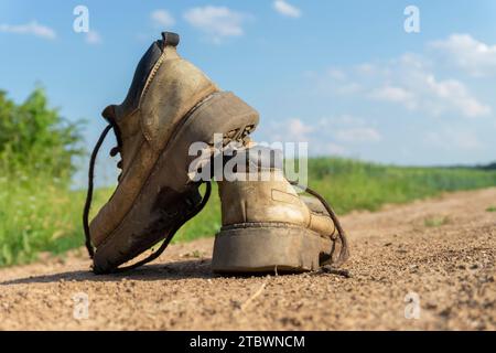 Paar alte, abgetragene Leder Wanderschuhe ein schotterweg oder Straße übereinander in der Nähe zu sehen, ausgeglichen Stockfoto