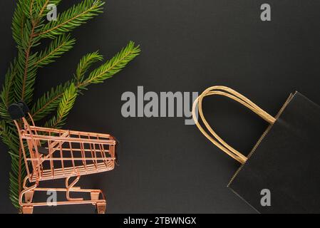 Tannenzweig, Einkaufswagen und Einkaufstasche aus schwarzem Papier auf schwarzem Hintergrund mit Kopierraum für Text, flache Schablone mit Draufsicht. Black Friday-Angebot Stockfoto
