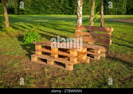 Gartenmöbel aus Holzpaletten, umgeben von Bäumen und Grün in der Sommersonne Stockfoto