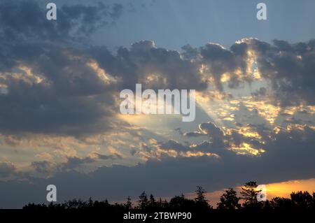 Glühende Sonne späht bei Sonnenuntergang in einem dämmerungsblauen Himmel in einem Natur- oder Wetterhintergrund mit Kopierraum durch die Wolken Stockfoto