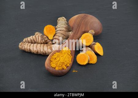 Kurkumapulver in Holzlöffel und (Curcuma longa Linn) Rhizom auf dunklem Hintergrund Stockfoto