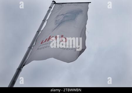 Neuruppin, Deutschland. Dezember 2023. Vor dem Universitätsklinikum Ruppin-Brandenburg fliegt eine Flagge mit der Abkürzung UKB. Als großes Krankenhaus in Brandenburg hat das Universitätsspital Neuruppin die Schließung zweier Fachabteilungen Anfang 2024 angekündigt. Quelle: Carsten Koall/dpa/Alamy Live News Stockfoto