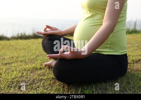 Schwangere Frau, die Yoga-Posen für Meditation am Strand macht Stockfoto