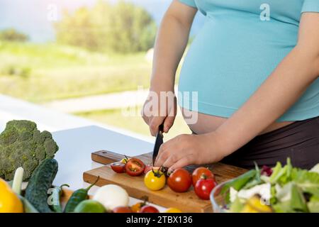 Eine schwangere Frau bereitet ein Salatgericht am Tisch zu Stockfoto
