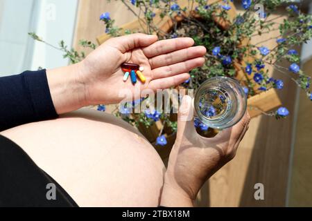 Pillen und Wasserbecher in die Hände einer schwangeren Frau Stockfoto