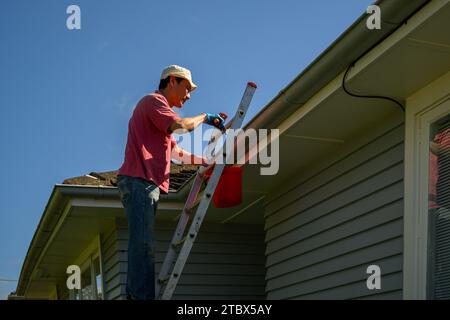 Mann, der auf der Leiter steht und die Rinne reinigt. Hauswartungsarbeiten. Auckland. Stockfoto